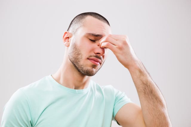 Portrait of young man who is having pain in his sinus.