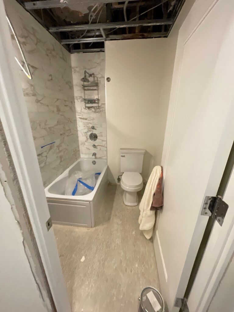 Restored bathroom after water damage, featuring a new bathtub, marble tile walls, and fresh drywall installation.