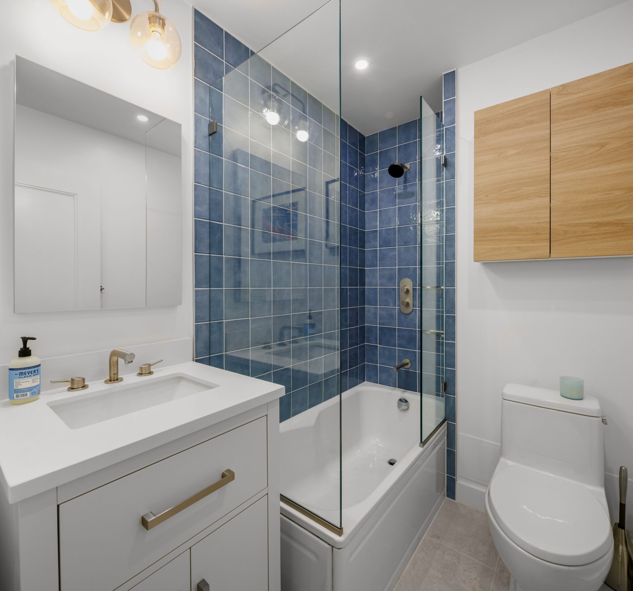 Modern bathroom renovation featuring blue ceramic tiles, a floating glass shower panel, and a sleek white vanity.