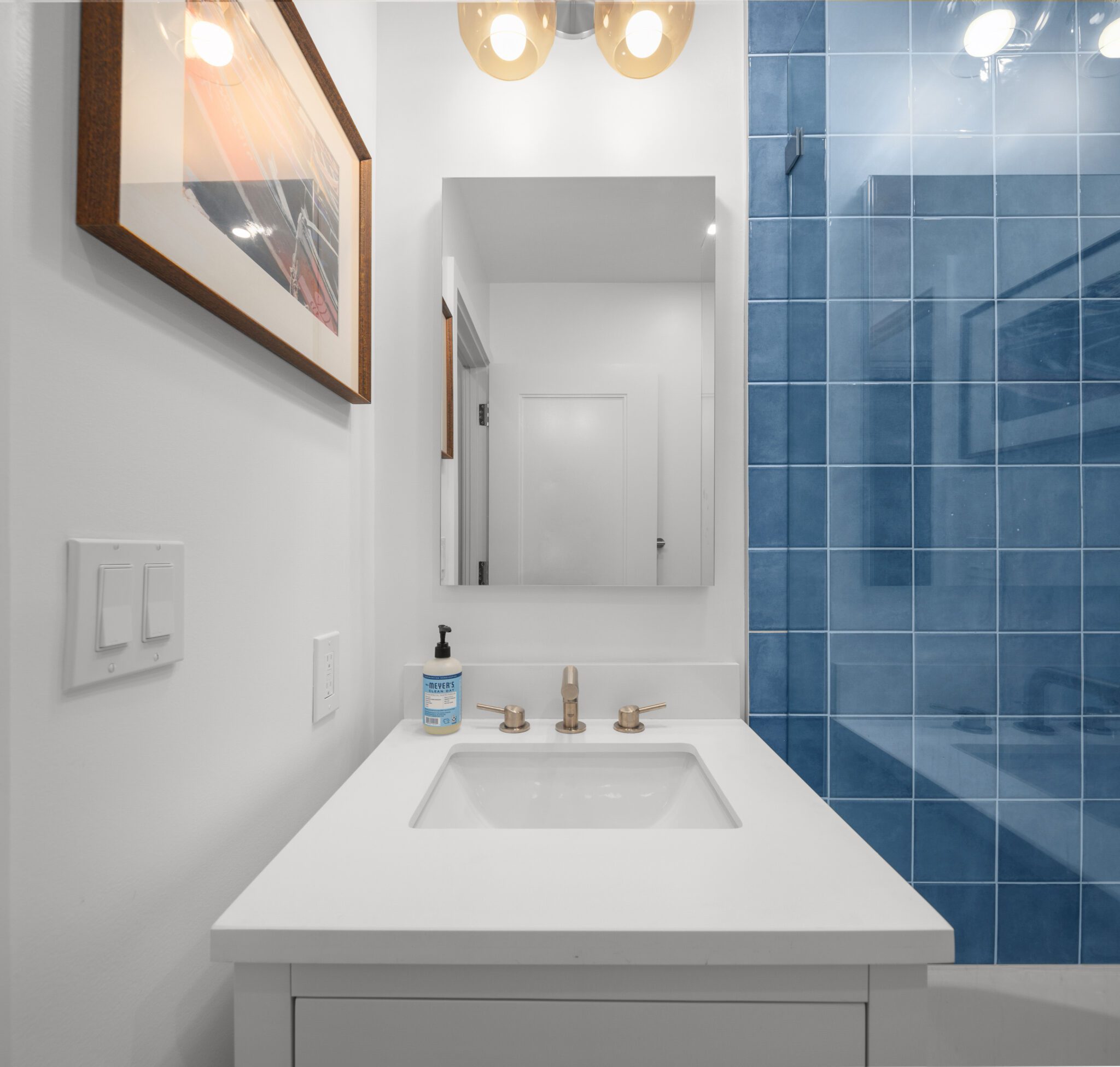 Close-up of a modern bathroom vanity with a white quartz countertop, gold faucet, and illuminated mirror.