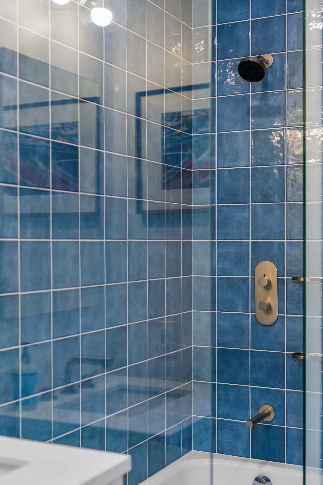 Luxurious blue-tiled shower with a built-in storage niche and gold fixtures for a sleek, modern aesthetic.