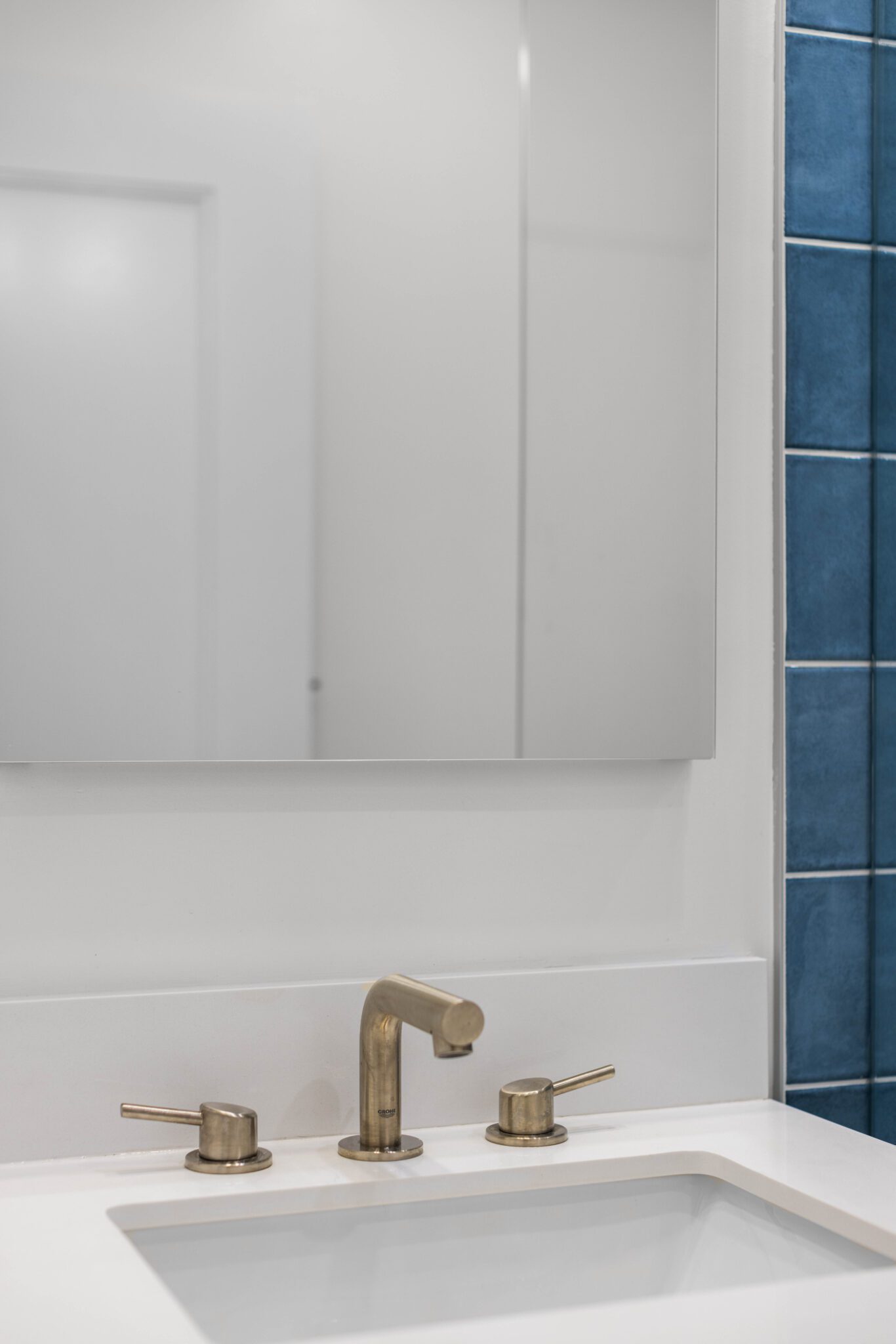 Close-up of a modern bathroom vanity with a white quartz countertop, gold faucet, and illuminated mirror.