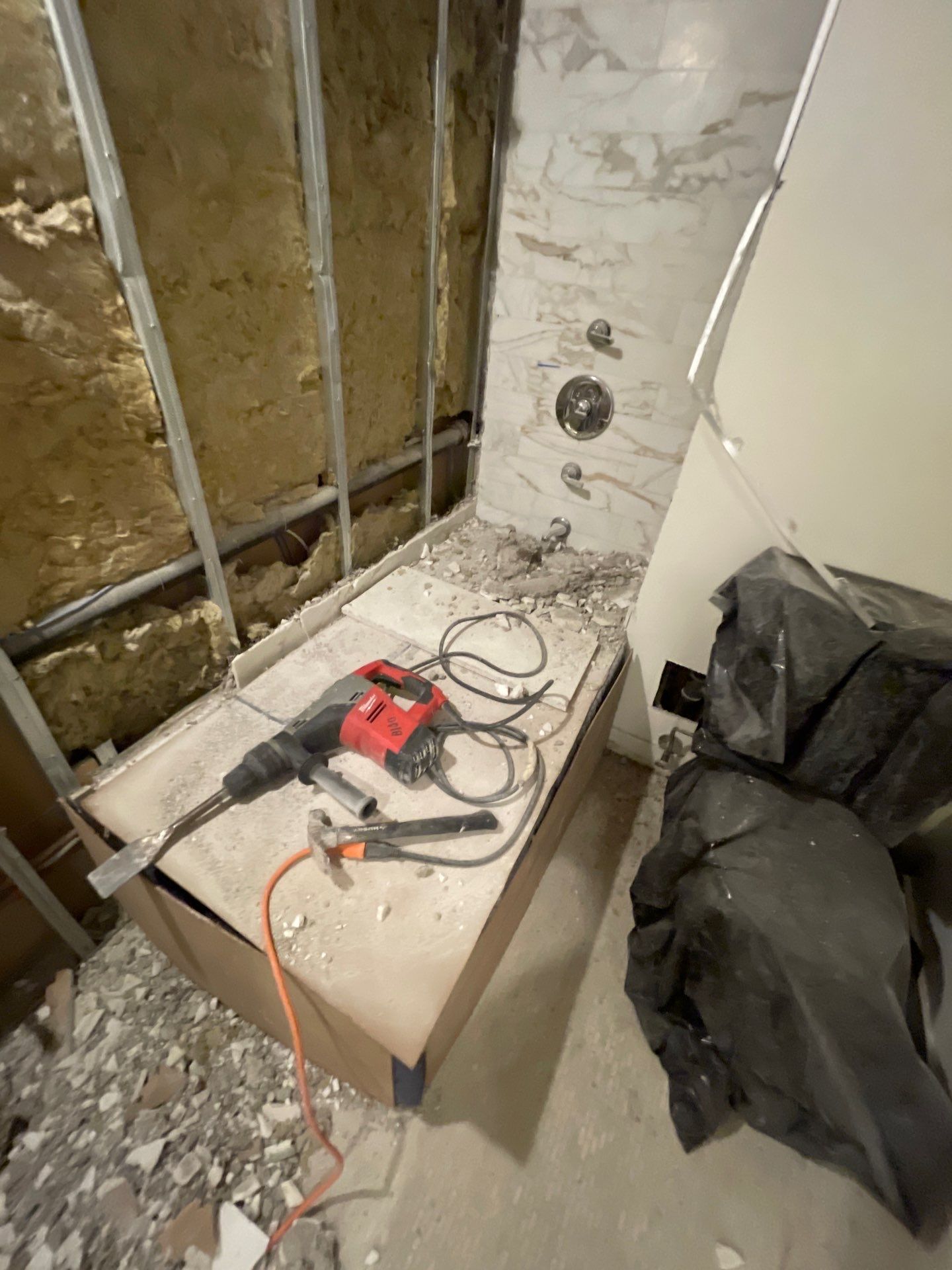 Bathroom under renovation after water damage, showing exposed wall studs, insulation, and partially demolished bathtub area.