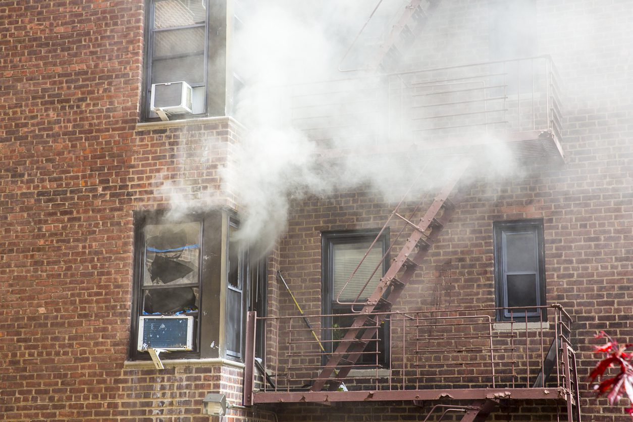 An old apartment is on fire with smoke coming out from the window.