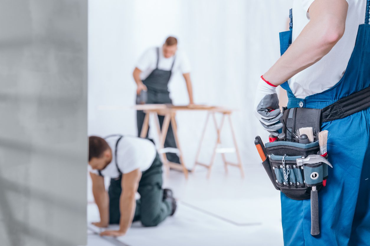 Close-up of handyman with glove on hand and tool belt on blue trousers during home renovation
